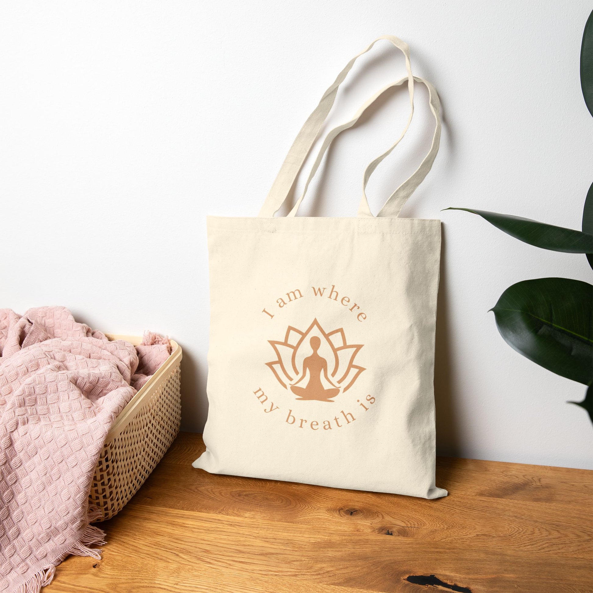 Beige tote bag with motivational quote on a wooden surface with a plant in the background