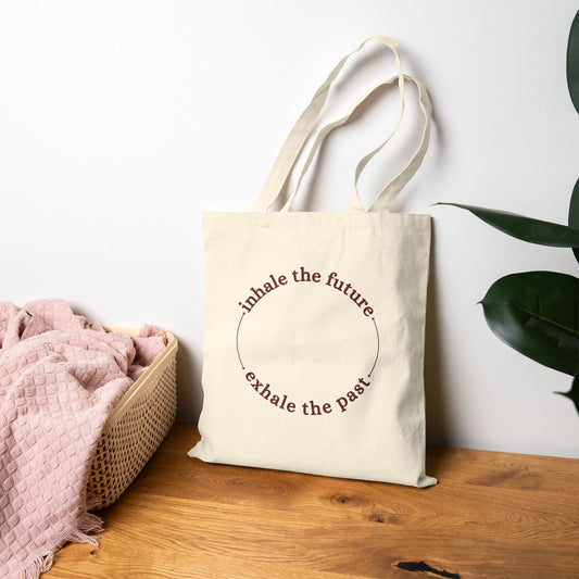 Beige tote bag with text on a wooden surface with a white wall and plant in the background